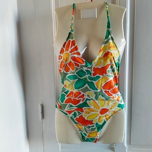 Può includere: Un costume da bagno con stampa floreale verde, arancione e giallo con uno stile a halter.