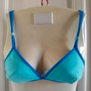 May include: A light blue triangle-shaped bra with a blue trim. The bra has adjustable straps with a small blue bead on each strap.