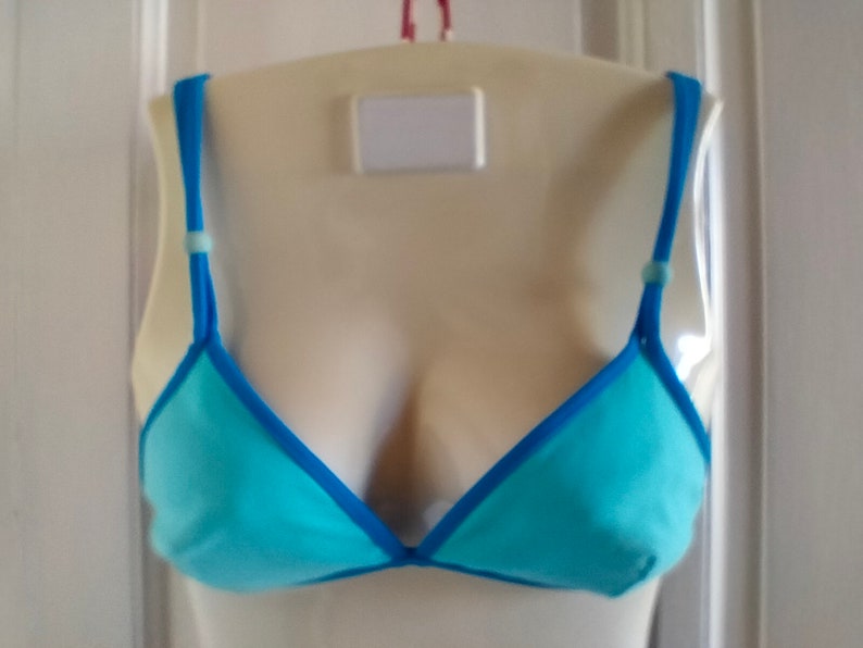 May include: A light blue triangle-shaped bra with a blue trim. The bra has adjustable straps with a small blue bead on each strap.