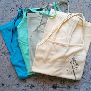 May include: Four sleeveless shirts in different colors: light blue, turquoise, mint green, and cream. The cream shirt has a palm tree design.