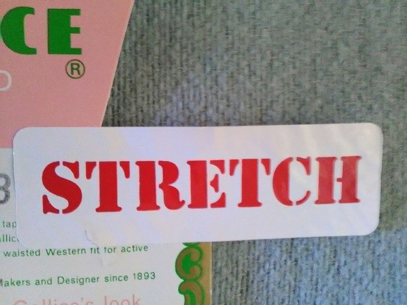 May include: White label with the word "STRETCH" printed in red letters. The label is attached to a pink and green fabric with the text "CE" and "Makers and Designer since 1893".