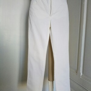 May include: White denim jeans with a straight leg fit. The jeans have a classic five-pocket style and a button fly.