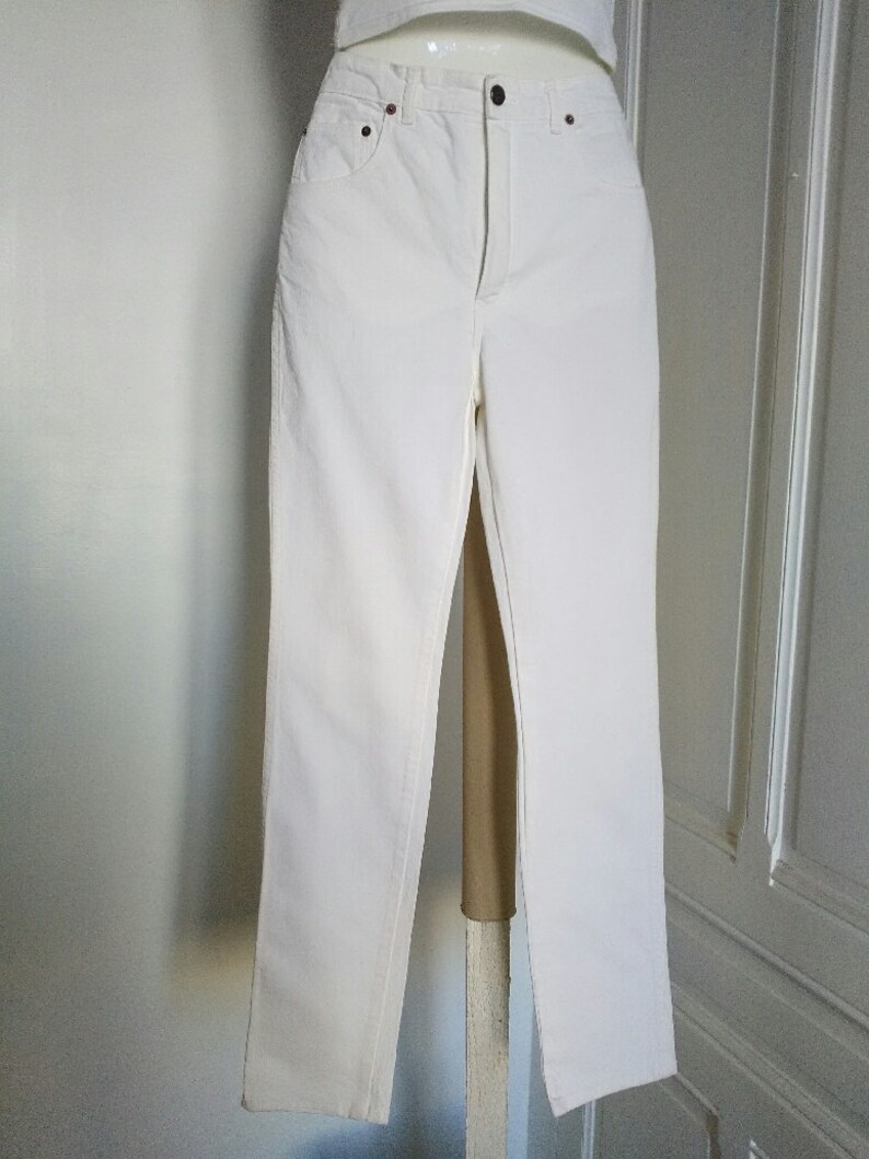 May include: White denim jeans with a straight leg fit. The jeans have a classic five-pocket style and a button fly.