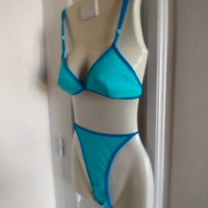 May include: A turquoise blue bikini top and bottom with a bright blue trim. The bikini is displayed on a white mannequin.