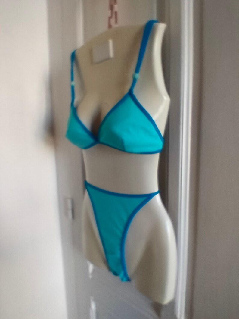 May include: A turquoise blue bikini top and bottom with a bright blue trim. The bikini is displayed on a white mannequin.