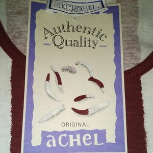 May include: A white and burgundy striped shirt with a tag that reads "Authentic Quality - Original aCHEL" and features a purple border and a graphic of five white and burgundy worms.