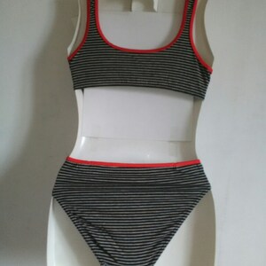 May include: Black and white striped bikini top and bottom with red trim. The bikini is on a white mannequin.