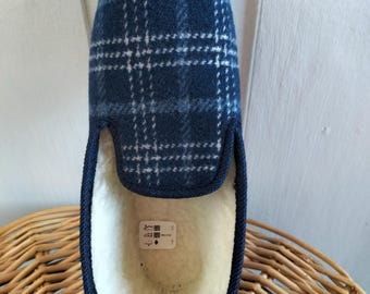 Puede incluir: Una zapatilla tipo pantufla con un patrón de cuadros en azul oscuro y azul claro en el exterior. El interior está forrado con un material de forro polar sintético de color crema. Una pequeña etiqueta blanca es visible en el talón.