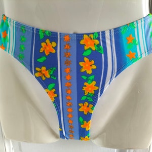 Op de afbeelding: Blauw en wit gestreepte bikini onderkant met een bloemenprint met gele bloemen en groene bladeren.