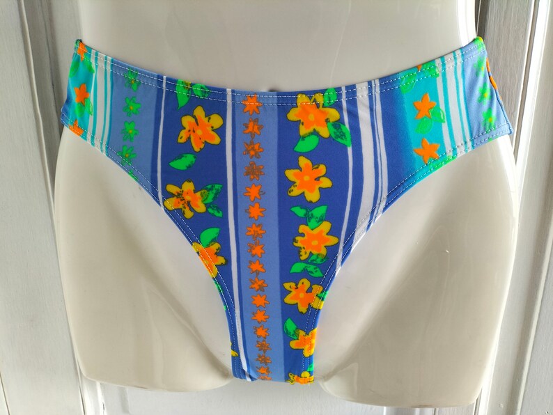 Op de afbeelding: Blauw en wit gestreepte bikini onderkant met een bloemenprint met gele bloemen en groene bladeren.