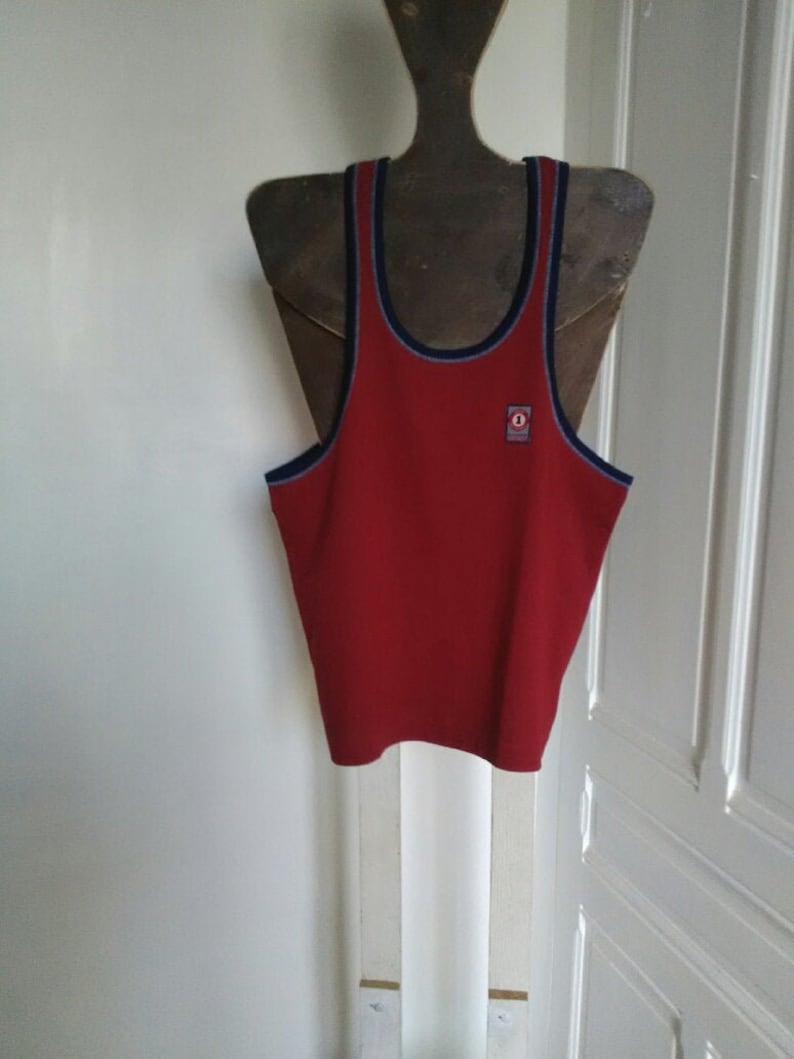 May include: Red sleeveless shirt with a blue and white trim around the neck and armholes. A small logo is on the front of the shirt.