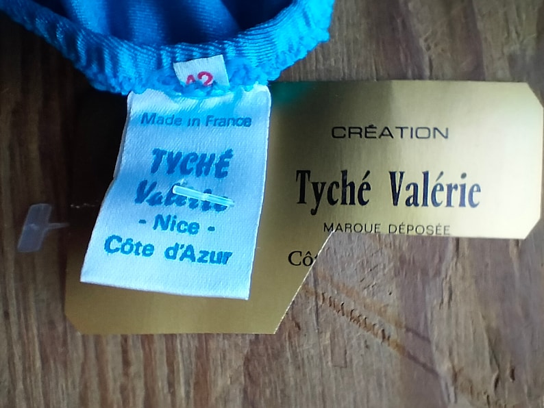 May include: A white tag with blue text that reads "Made in France" and "Tyche Valerio - Nice - C&ocirc;te d'Azur". A gold tag with black text reads "Creation Tyche Val&eacute;rie Marque D&eacute;pos&eacute;e".