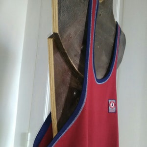 May include: Red sleeveless tank top with a blue trim and a small circular patch with the number "1" on the front.