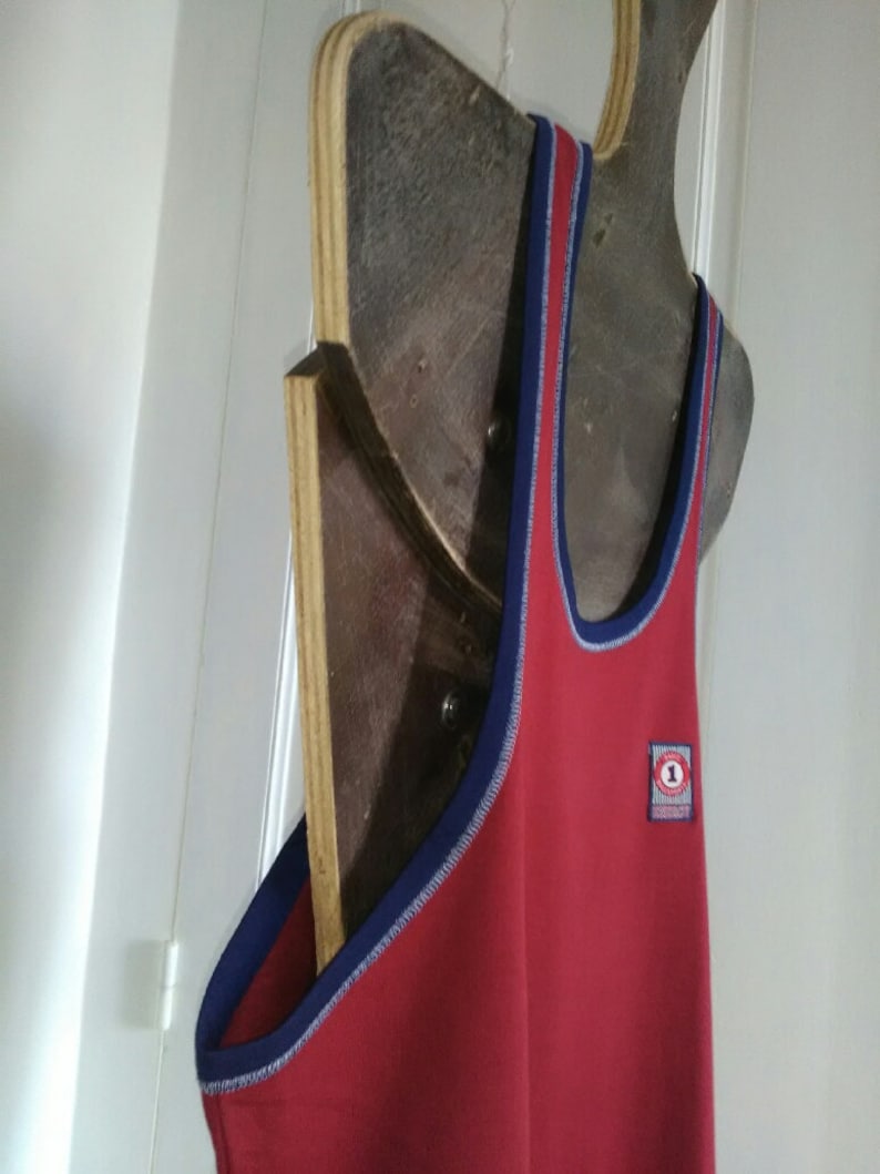 May include: Red sleeveless tank top with a blue trim and a small circular patch with the number "1" on the front.