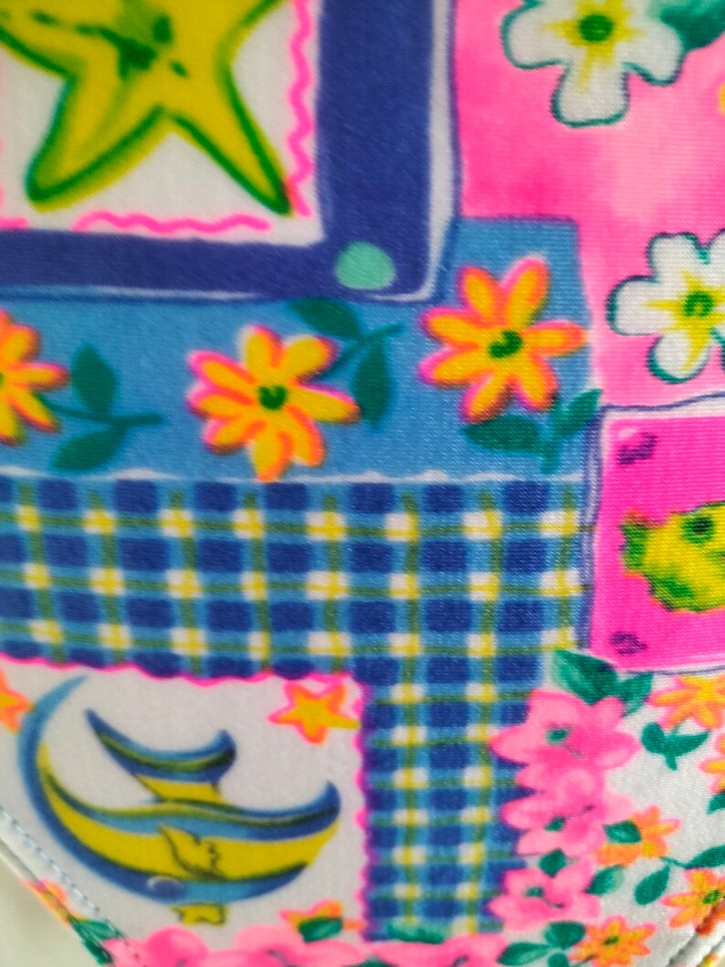 Puede incluir: Primer plano de una tela colorida con un dise&ntilde;o de patchwork. El patr&oacute;n incluye cuadrados azules, rosas y blancos con estrellas amarillas, flores y una luna creciente. La tela tiene un patr&oacute;n de cuadros y bordes florales.
