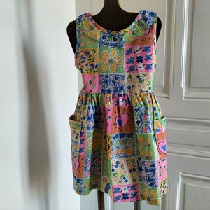 Peut inclure: Une robe sans manches en patchwork rose, vert et bleu avec un col blanc et deux poches. La robe a un motif floral et des cœurs.