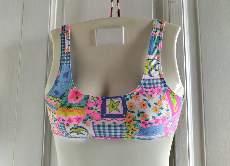 Puede incluir: Top de bikini patchwork colorido con una variedad de patrones, incluyendo motivos florales, cuadros y n&aacute;uticos. El top presenta una mezcla de colores rosa, azul, amarillo y blanco. Las correas y los bordes son rosas.