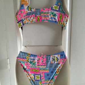 Puede incluir: Un traje de ba&ntilde;o de dos piezas con un dise&ntilde;o de patchwork vibrante. La parte superior e inferior presentan una mezcla de motivos florales, caballitos de mar y peces en rosa, azul y amarillo. El traje de ba&ntilde;o se exhibe en un maniqu&iacute;.