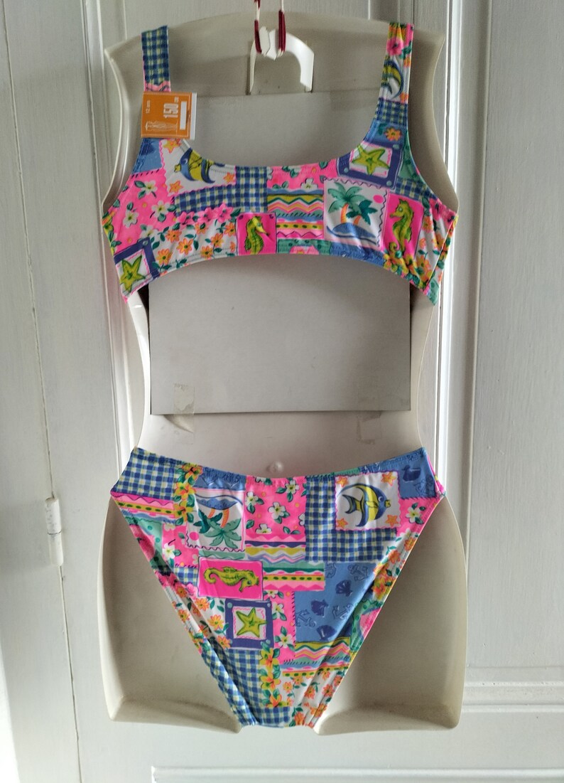 Puede incluir: Un traje de ba&ntilde;o de dos piezas con un dise&ntilde;o de patchwork vibrante. La parte superior e inferior presentan una mezcla de motivos florales, caballitos de mar y peces en rosa, azul y amarillo. El traje de ba&ntilde;o se exhibe en un maniqu&iacute;.