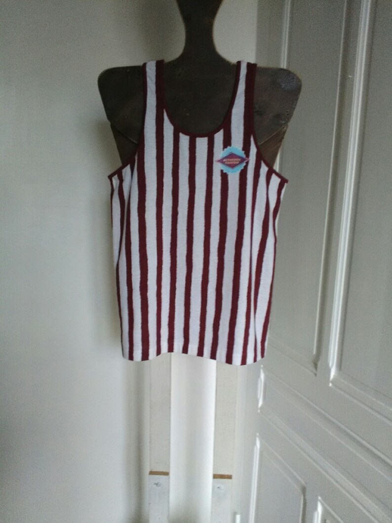 May include: White and maroon striped tank top with a small blue and pink diamond-shaped patch that says "EST. 1989" on the front.