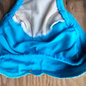 May include: A turquoise blue swimsuit top with gold trim and a white lining. The top is made of a soft, stretchy fabric.