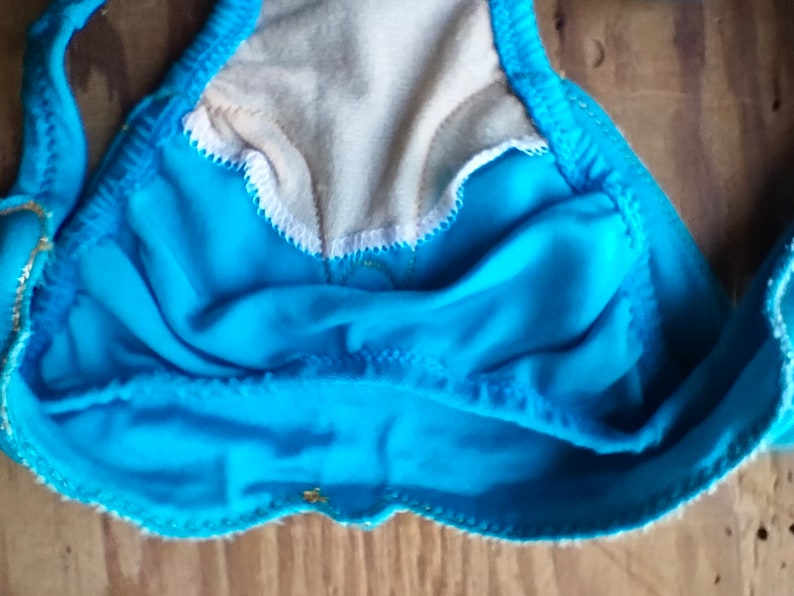 May include: A turquoise blue swimsuit top with gold trim and a white lining. The top is made of a soft, stretchy fabric.