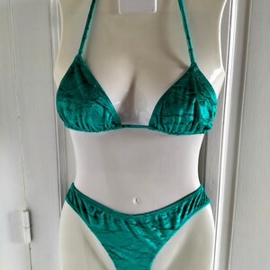 May include: A teal green bikini with a triangle top and a high-cut bottom. The bikini is made of a textured fabric.