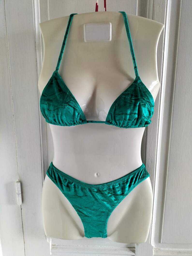 May include: A teal green bikini with a triangle top and a high-cut bottom. The bikini is made of a textured fabric.