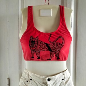 Peut inclure: Top de réservoir rouge avec un motif noir et blanc d'un animal stylisé avec des taches. Le débardeur est sur un mannequin blanc.