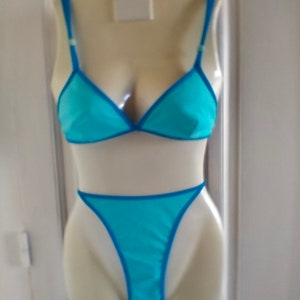 May include: A turquoise blue lingerie set with a triangle bra and a thong. The lingerie has a blue trim.