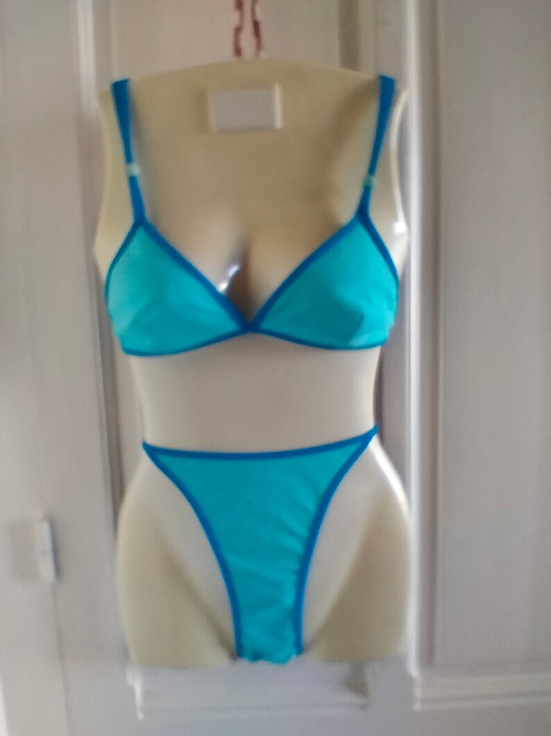 May include: A turquoise blue lingerie set with a triangle bra and a thong. The lingerie has a blue trim.