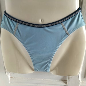 Op de afbeelding: Lichtblau ondergoed met een donkerblauwe rand en decoratieve stiksels. Het ondergoed wordt op een mannequin getoond. Het kledingstuk heeft een lage taille en een gladde, zijdeachtige textuur.