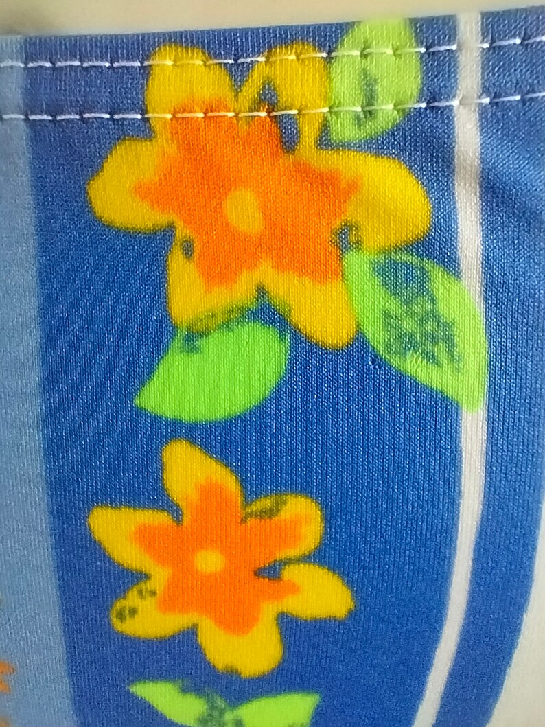 Op de afbeelding: Close-up van een blauwe stof met een witte streep en een herhalend patroon van oranje en gele bloemen met groene bladeren.
