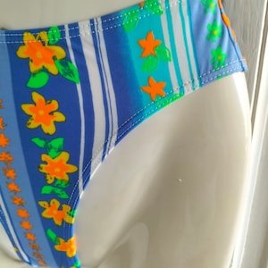 Op de afbeelding: Blauw en wit gestreepte bikini onderkant met een bloemenprint met oranje en groene bloemen.