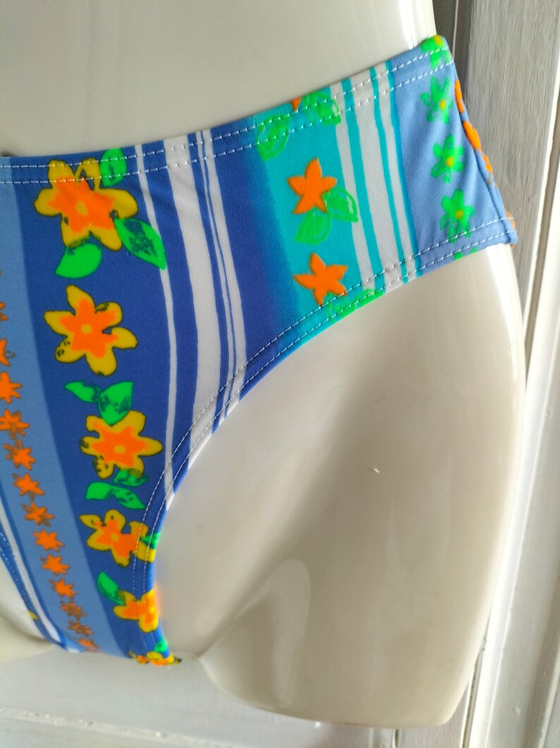 Op de afbeelding: Blauw en wit gestreepte bikini onderkant met een bloemenprint met oranje en groene bloemen.