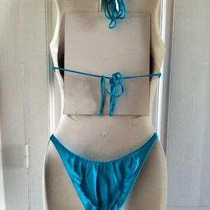 May include: A turquoise bikini bottom on a white mannequin. The bikini bottom is made of a smooth, silky fabric.
