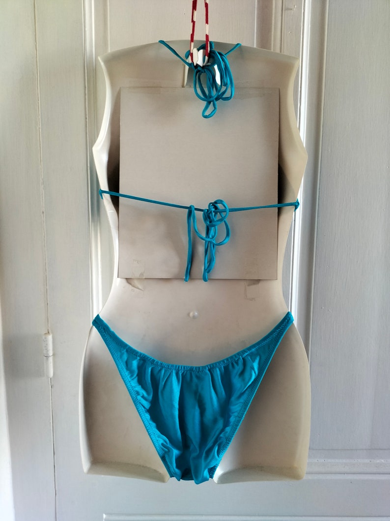 May include: A turquoise bikini bottom on a white mannequin. The bikini bottom is made of a smooth, silky fabric.