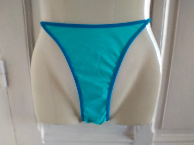 May include: Light blue lingerie with a turquoise trim. The lingerie is made of a sheer fabric and has a low-cut back.