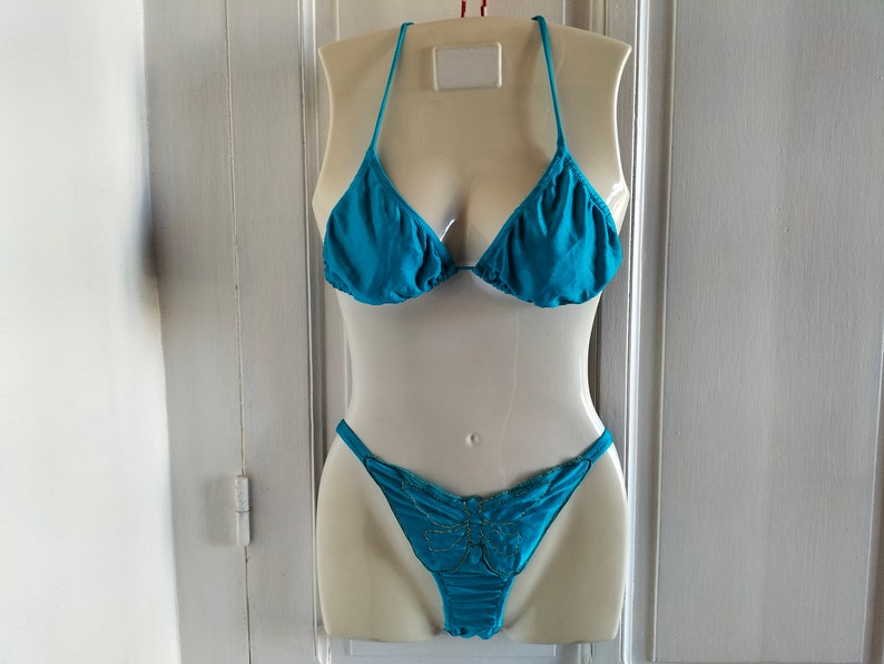 May include: Teal blue bikini top and bottom with a butterfly design on the bottom. The bikini is displayed on a white mannequin.