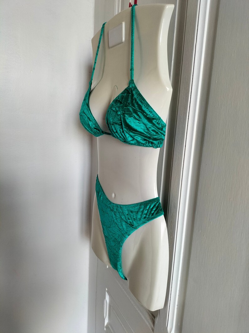 May include: Teal green velvet bikini top and bottom. The top is a triangle style with thin straps. The bottom is a high-cut style with a small amount of fabric covering the rear.