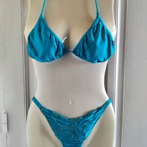 May include: A turquoise bikini top and bottom with a butterfly design on the bottom. The butterfly is outlined in gold.