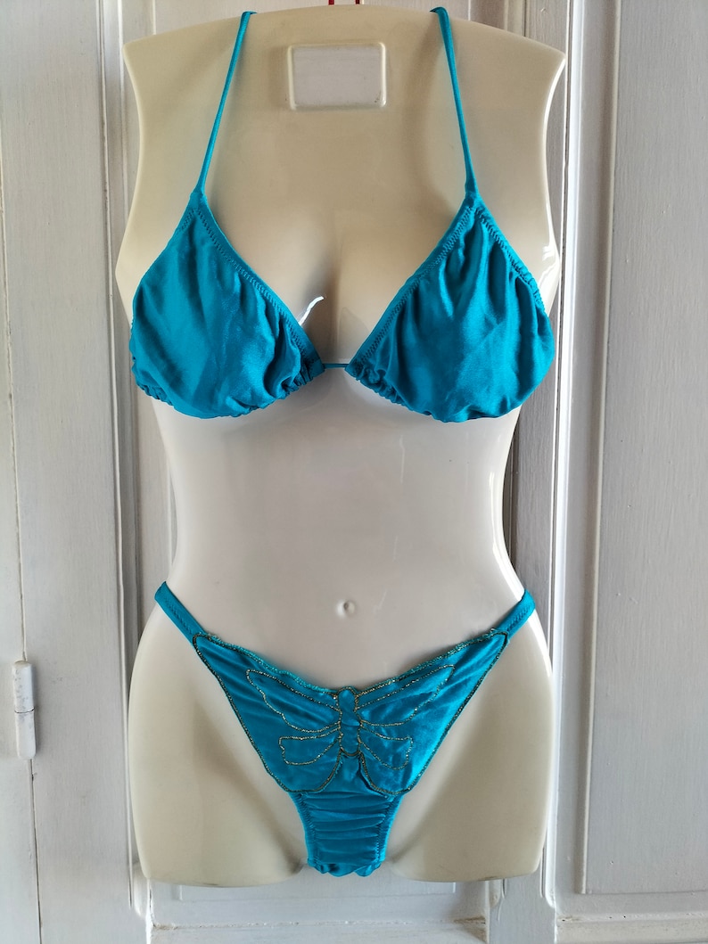 May include: A turquoise bikini top and bottom with a butterfly design on the bottom. The butterfly is outlined in gold.