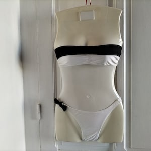 K&ouml;nnte beinhalten: Wei&szlig;er, tr&auml;gerloser Bikini-Oberteil mit schwarzem Band und einem passenden wei&szlig;en Unterteil mit schwarzer Schleife.