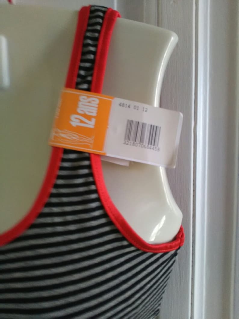 May include: A black and white striped tank top with red trim. The tank top has a tag that says "12 ans" and a barcode.
