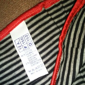 May include: A white tag with black text detailing the fabric composition of a striped garment. The tag reads: "12A, F 150, D 152, Cotton 95%, Cotton, Baumwolle, Katoen, Elasthanne, Elastane, 5% Elasthan, Polyurethaan, Elastomeer, Made in France."