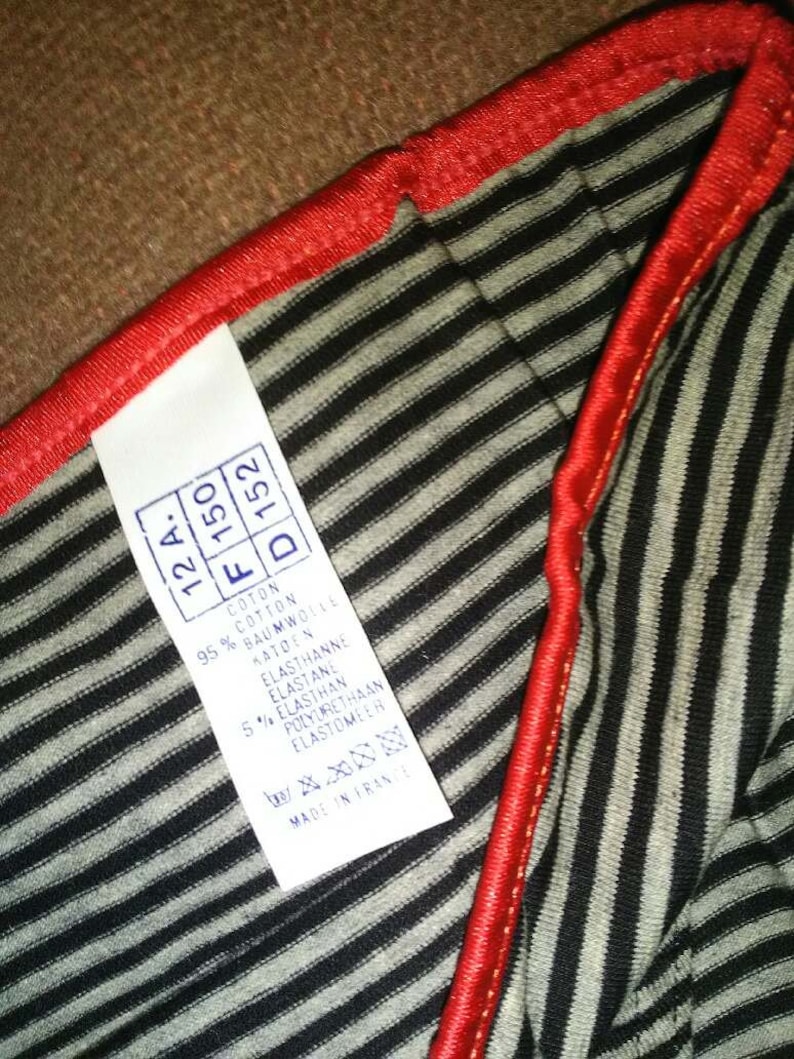 May include: A white tag with black text detailing the fabric composition of a striped garment. The tag reads: "12A, F 150, D 152, Cotton 95%, Cotton, Baumwolle, Katoen, Elasthanne, Elastane, 5% Elasthan, Polyurethaan, Elastomeer, Made in France."