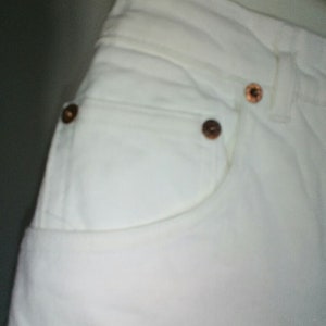May include: White denim jeans with a front pocket and copper-colored rivets.