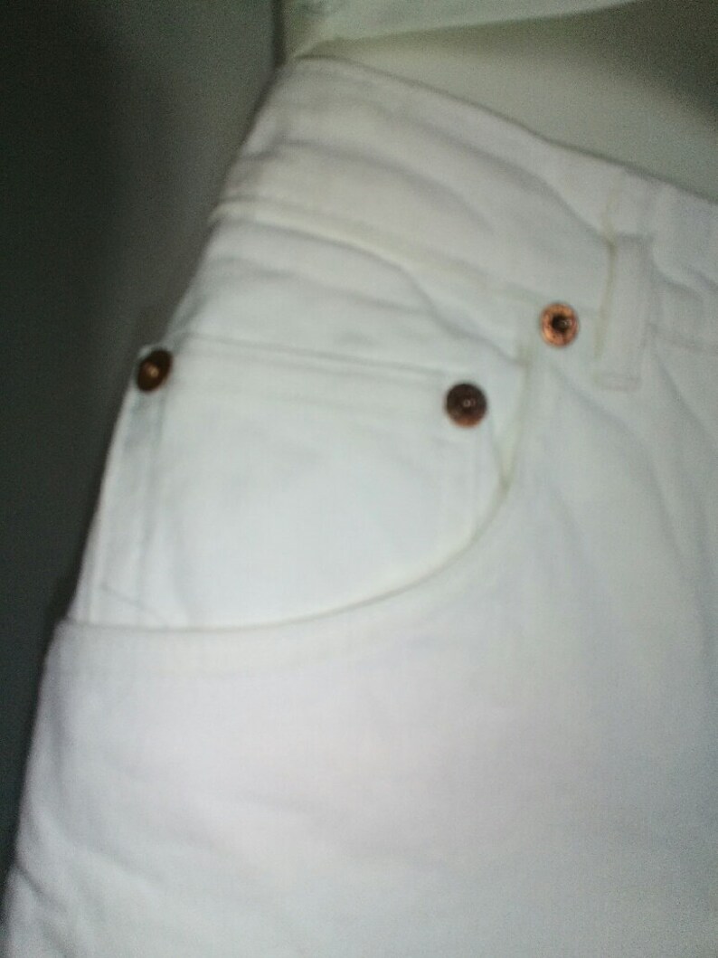 May include: White denim jeans with a front pocket and copper-colored rivets.
