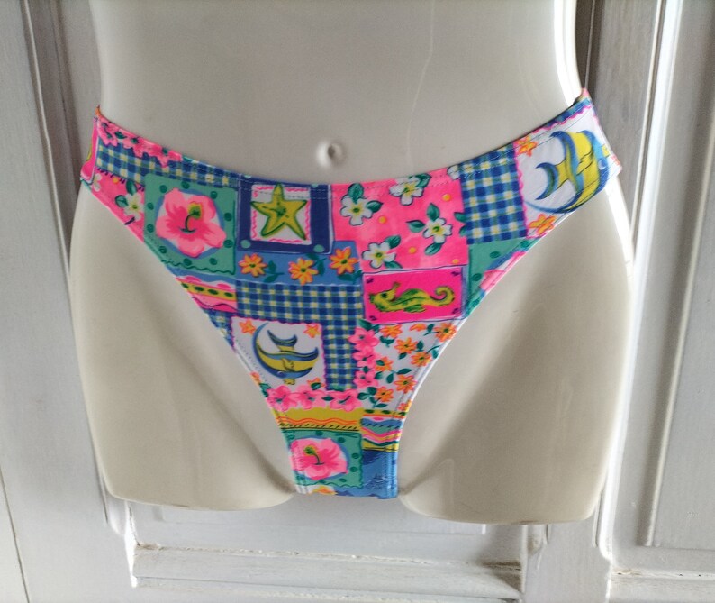 Puede incluir: Braguita de bikini colorida con un dise&ntilde;o de patchwork. La tela presenta motivos florales, de criaturas marinas y geom&eacute;tricos en tonos rosa, azul, verde y amarillo. La braguita de bikini se muestra en un maniqu&iacute;.