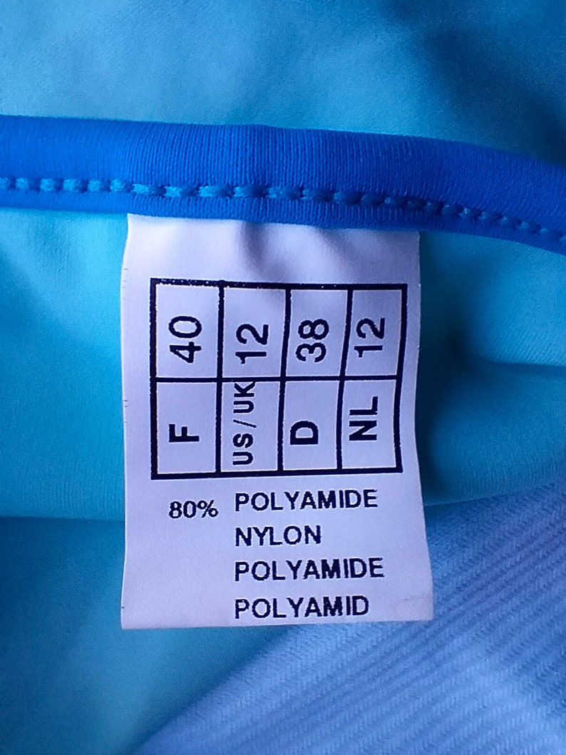 May include: A white tag with black text showing sizing information for a garment. The tag reads "F 40", "US/UK 12", "D 38", "NL 12". The tag also lists the fabric composition as 80% polyamide and 20% nylon.